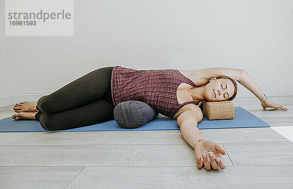 Junge Frau liegt auf der Seite und entspannt sich  während sie im Studio Yoga übt