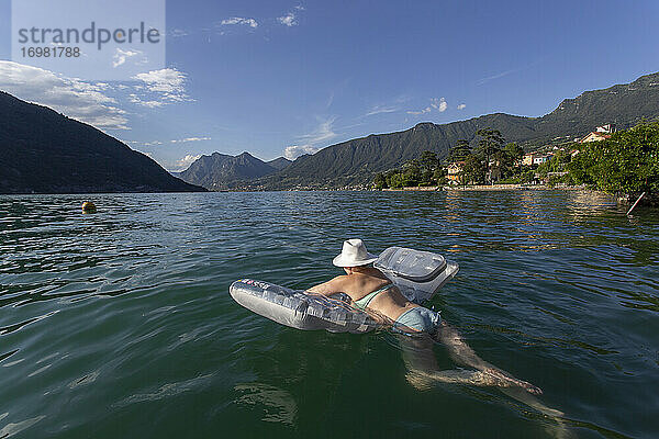 Eine weibliche Sonnenanbeterin schwimmt auf einem Floß im Iseosee  Italien