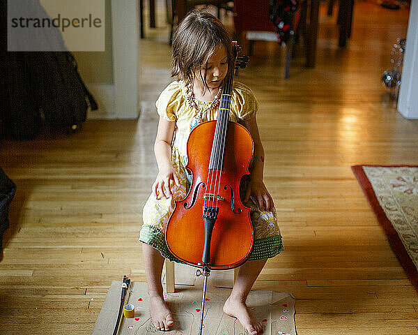 Draufsicht auf ein niedliches barfüßiges Kind im Fensterlicht  das ein kleines Cello hält