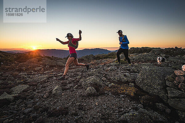 Mann und Frau beim Trailrunning mit Hund in den Bergen bei Sonnenaufgang