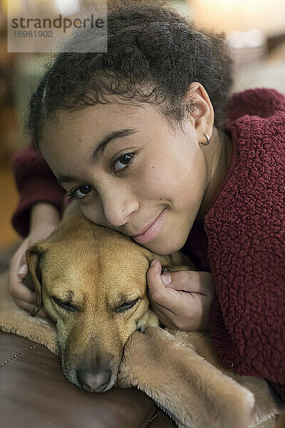 Porträt eines gemischtrassigen elfjährigen Mädchens  das mit einem kleinen braunen Hund kuschelt