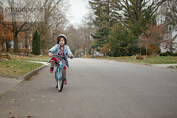 Ein kleines Mädchen in gestreiften Strumpfhosen und mit Helm fährt allein die Straße entlang