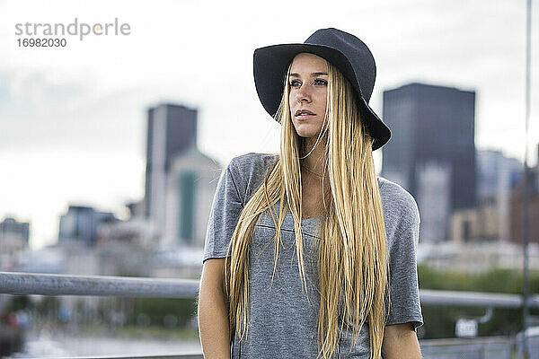 Blonde Frau mit Hut und Stadtsilhouette im Hintergrund