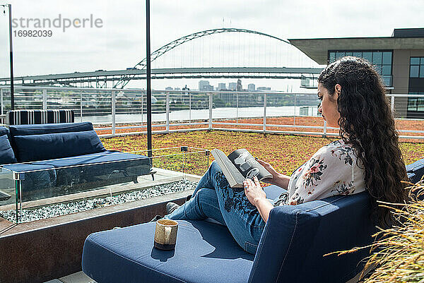 Frau liest ein Buch auf dem Dach draußen mit Brücke und Stadt