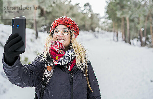 Lächelndes Mädchen genießt den Winter und macht ein Selfie bei Schneefall