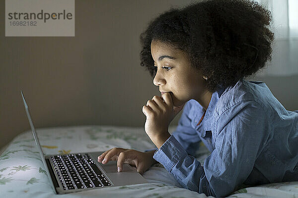 Seitenansicht eines zehnjährigen gemischtrassigen Mädchens bei der Arbeit an ihrem Laptop