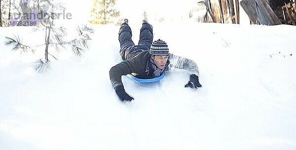 Mann rutscht in einem Schlitten einen verschneiten Hügel hinunter