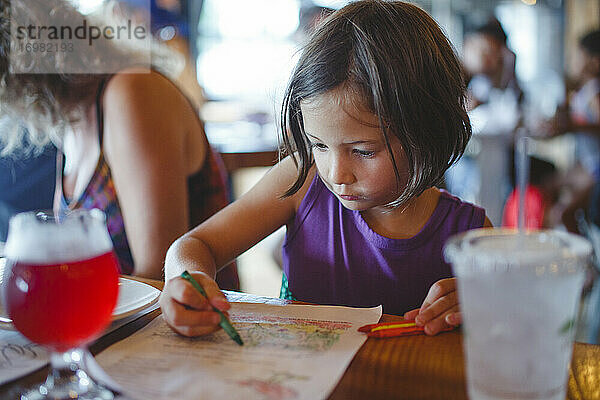 Ein kleines Mädchen sitzt an einem Restauranttisch und malt mit Buntstiften