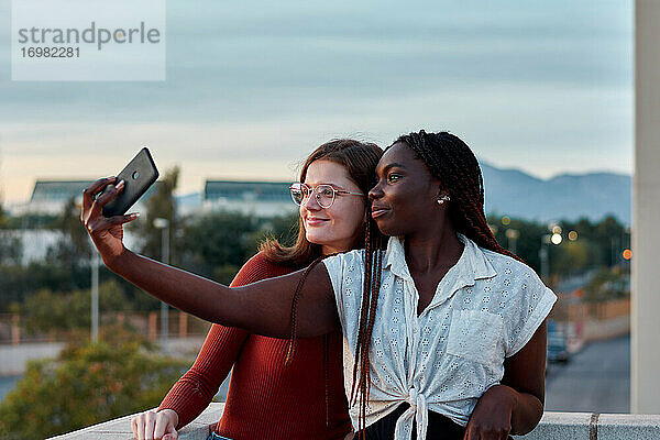 Zwei junge Frauen machen ein Selbstporträt mit ihrem Handy bei Sonnenuntergang