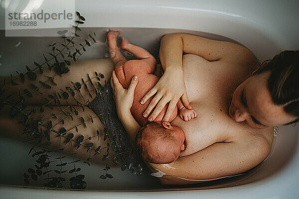 Draufsicht auf eine Mutter  die ihr neugeborenes Baby in der Badewanne stillt