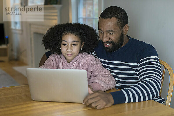 Ein afroamerikanischer Vater und seine gemischtrassige Tochter am Laptop