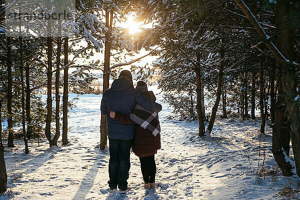 Paar stehend im Winterwald mit Blick auf den Sonnenuntergang in der Nähe des gefrorenen