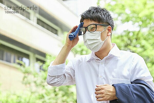 Junger japanischer Geschäftsmann mit Maske im heißen Sommer in der Innenstadt von Tokio
