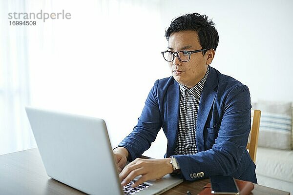 Junger japanischer Geschäftsmann arbeitet mit Laptop