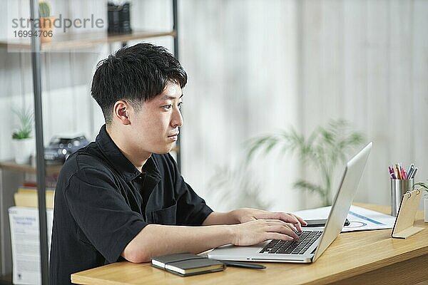 Junger japanischer Geschäftsmann arbeitet mit Laptop