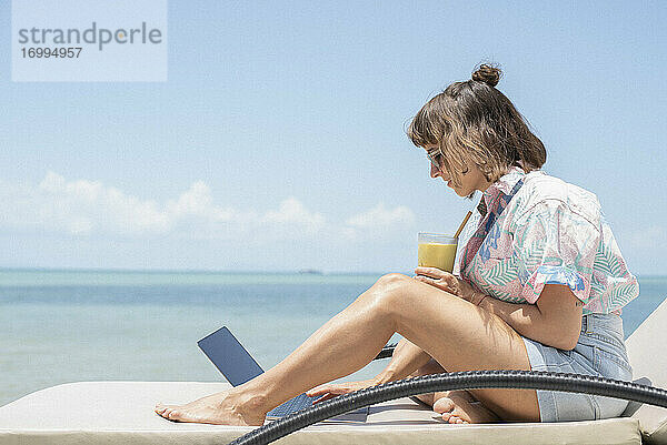 Frau mit Cocktail mit Laptop auf sonnigen Strand Liegestuhl