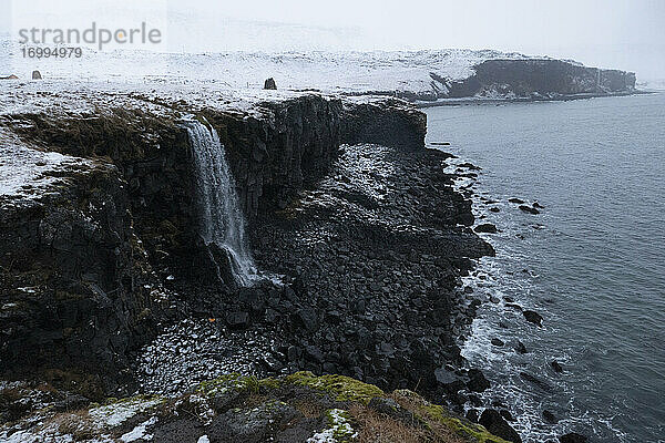 Majestätischer schneebedeckter Wasserfall über Meeresklippe  Arnastapi  Island