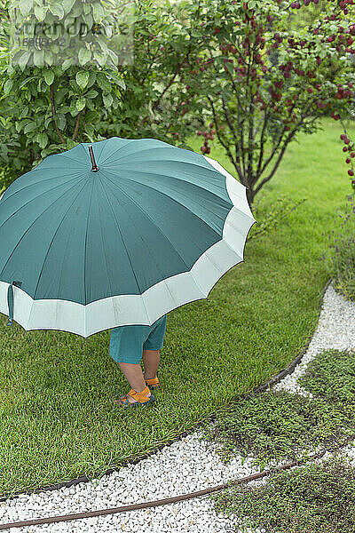 Kleinkind unter großem grünen Regenschirm im Garten