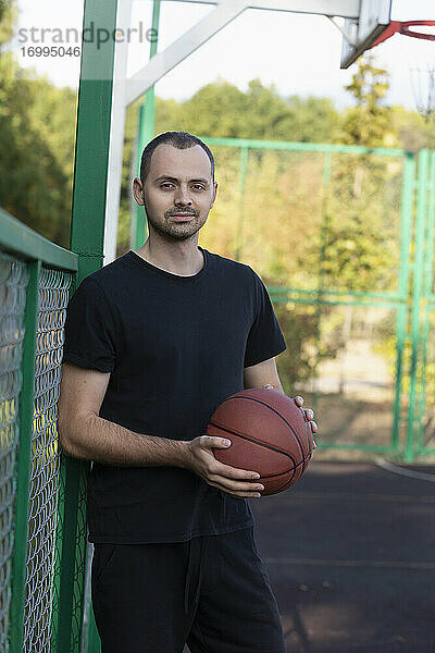 Porträt selbstbewusst junger Mann spielt Basketball im Park Basketballplatz