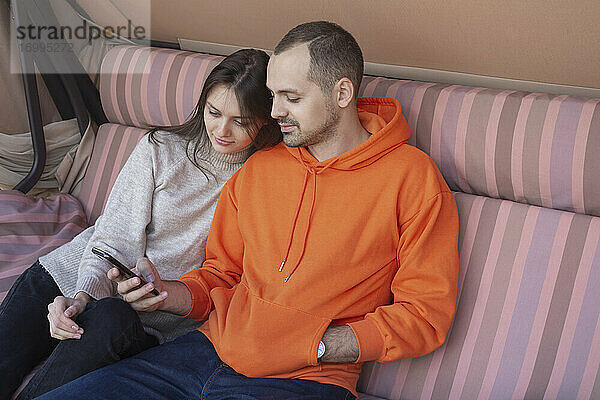 Junges Paar mit Smartphone auf der Terrassenschaukel