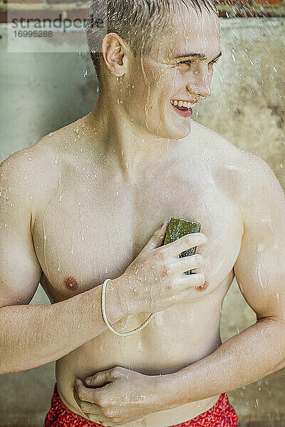 Glücklicher junger Mann mit Seife beim Duschen im Freien
