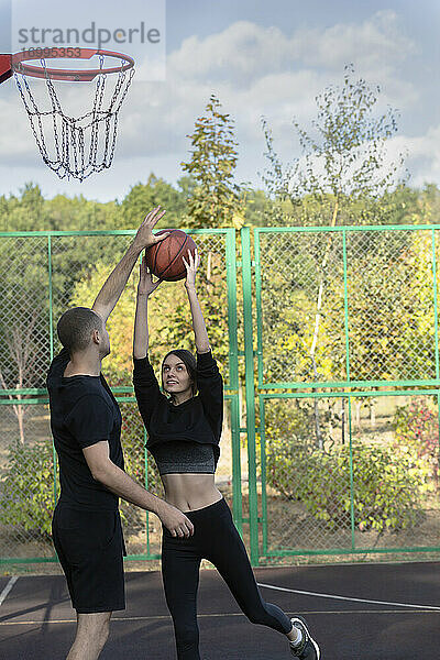 Junges Paar spielt Basketball im Park Basketballplatz