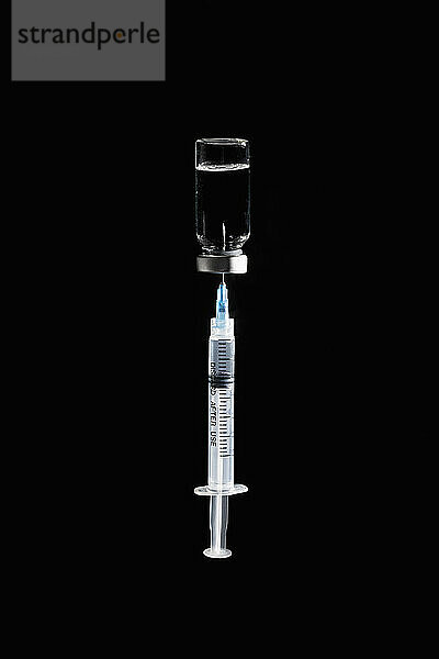 Spritze im COVID-19-Impfstoff-Fläschchen auf schwarzem Hintergrund