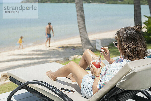 Frau genießt Cocktail auf sonnigen Strand Liegestuhl