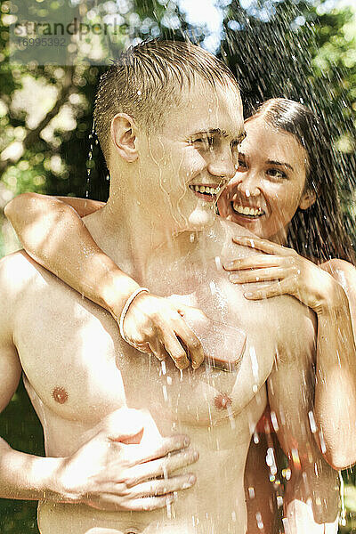 Glückliches junges Paar mit Seife duschen im Freien
