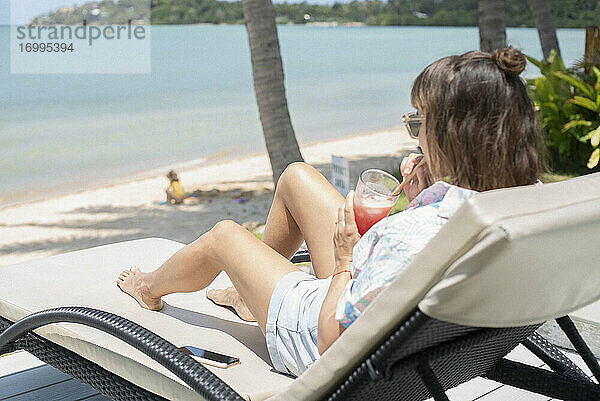 Frau trinken Cocktail auf sonnigen Strand Liegestuhl