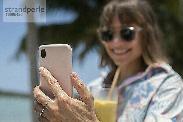 Glückliche Frau mit Cocktail nehmen Selfie am sonnigen Strand