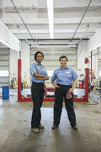 Porträt von zwei lächelnden Mechanikerinnen in einer Autowerkstatt.