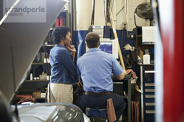 Mechaniker und Kunde schauen auf einen Computerbildschirm in einer Autowerkstatt
