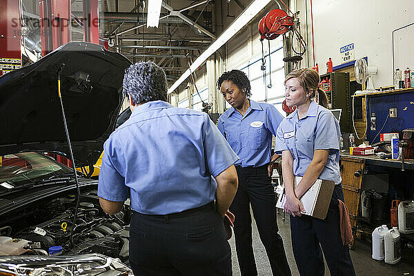 Drei Mechanikerinnen unterhalten sich und sehen sich den Motor eines Autos in einer Reparaturwerkstatt an