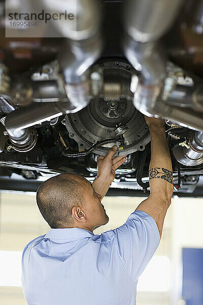 Ein Mechaniker aus einem pazifischen Inselstaat arbeitet an der Unterseite eines Fahrzeugs auf einer Hebebühne in einer Autowerkstatt