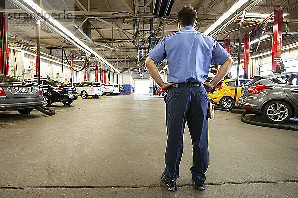 Automechaniker in einer Werkstatt  Rückansicht Mann mit Händen in den Hüften