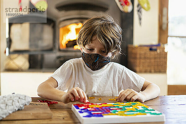 Junge mit Maske spielt Brettspiel zu Hause