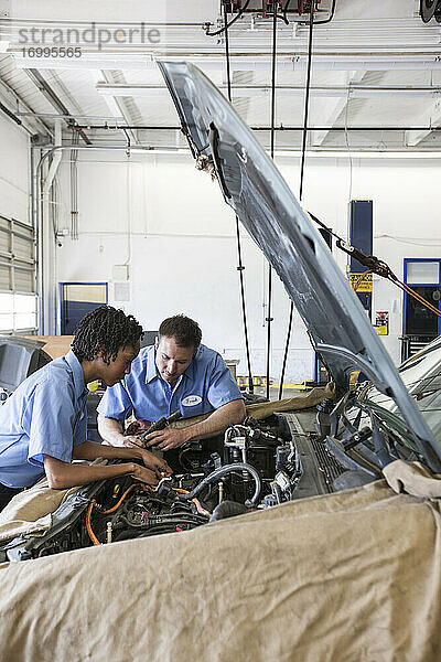 Männliche und weibliche Mechaniker unterhalten sich  während sie sich den Motor in einer Autowerkstatt ansehen