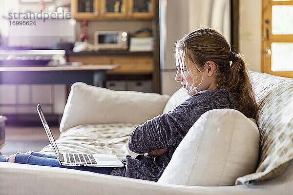 Teenager-Mädchen schaut auf Laptop auf Sofa