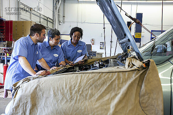 Drei Mechaniker teilen sich ein digitales Tablet und planen die Arbeit an einem Auto  das zur Reparatur ansteht