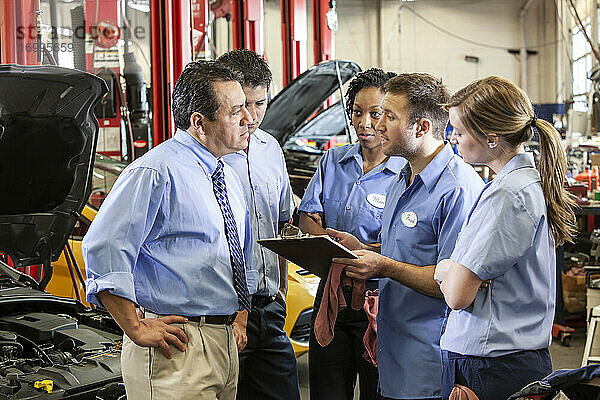 Ein Team von Mechanikern  die an einem Auto arbeiten  diskutiert ein Problem in einer Autowerkstatt