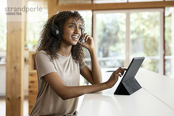 Geschäftsfrau mit digitalem Tablet  die über Kopfhörer spricht  während sie zu Hause sitzt
