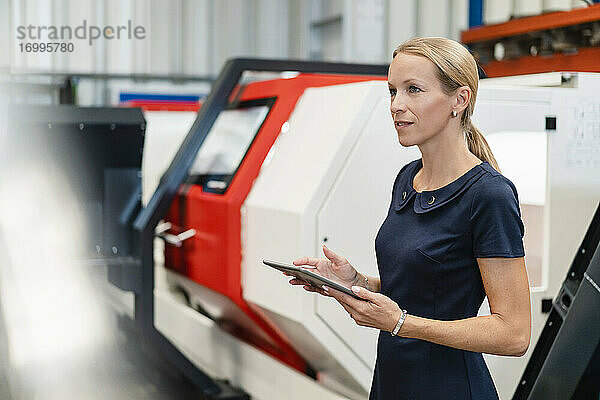 Blonde Geschäftsfrau mit digitalem Tablet vor Maschinen in der Industrie