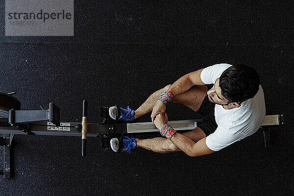 Sportler macht eine Pause  während er auf dem Rudergerät im Fitnessstudio sitzt