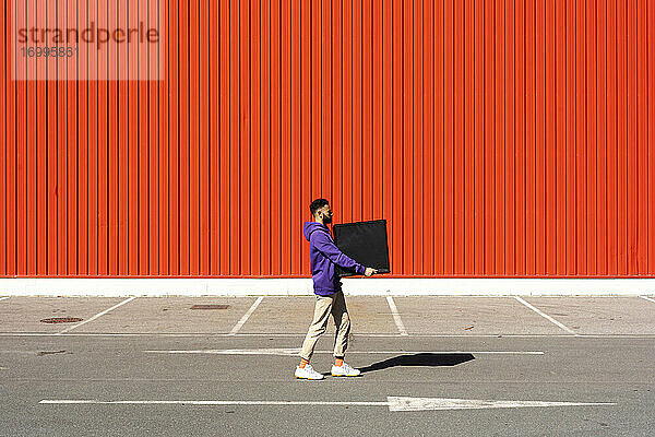 Junger Mann trägt eine Kiste vor einer roten Wand