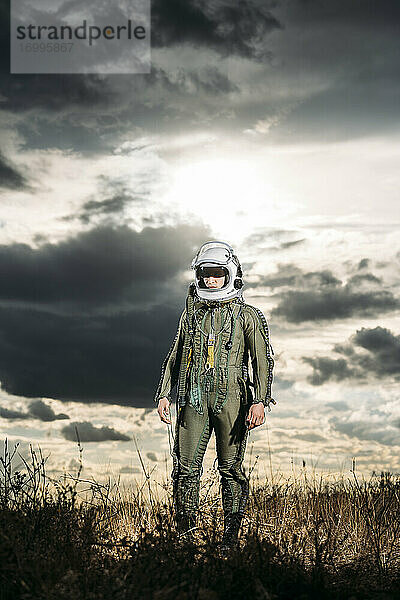 Mann posiert als Astronaut verkleidet auf einer Wiese mit dramatischen Wolken im Hintergrund