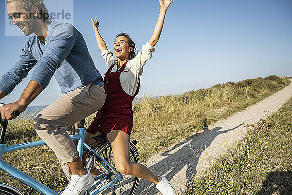 Unbekümmerte Frau genießt Fahrradfahrt mit Mann gegen klaren Himmel