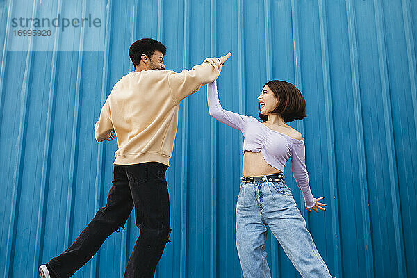 Glückliches Paar gibt sich High-Five  während es an einer blauen Wand steht