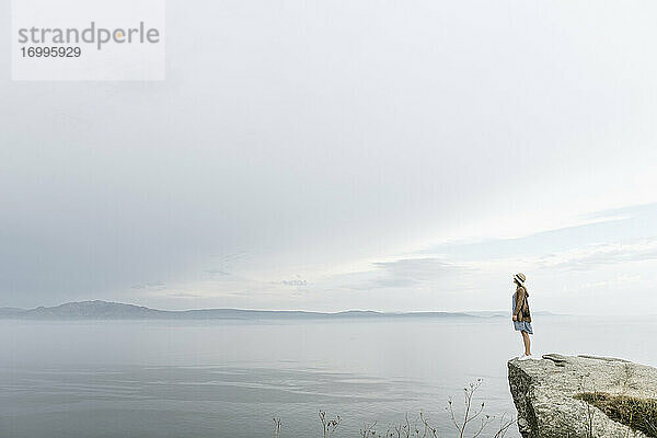 Frau steht auf einem Felsen und blickt auf das Meer