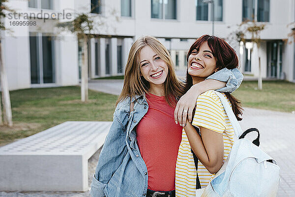 Fröhliche junge Frau mit Arm um Freundin auf dem Universitätscampus